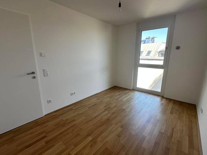 Unmöbliertes Zimmer mit Parkettboden, großen Fenstern und viel Tageslicht.