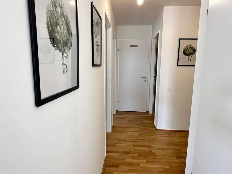 Heller Flur mit Holzboden, weißen Wänden und modernen Bildern an der Wand.