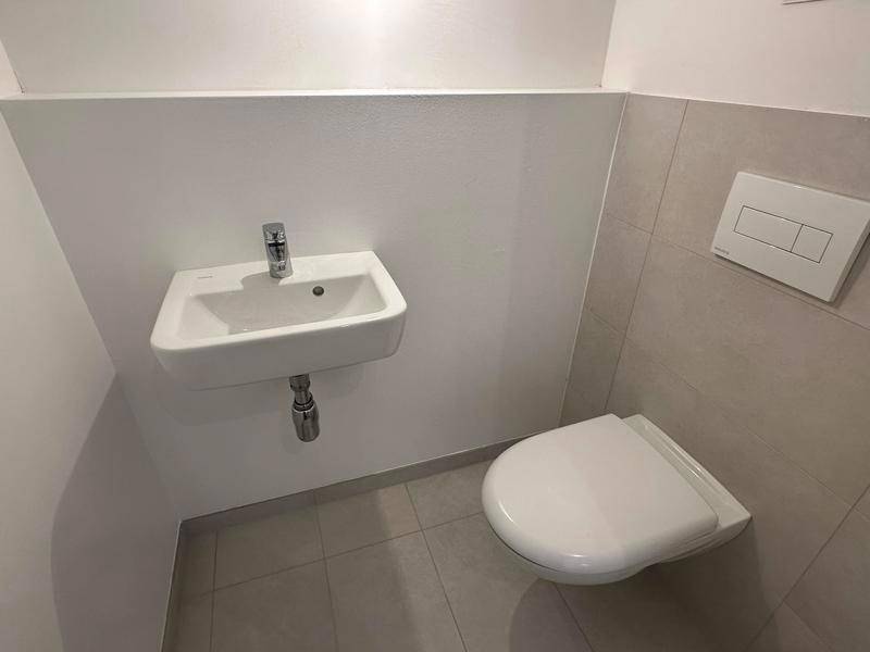 Kompaktes Gäste-WC mit wandhängender Toilette und kleinem Waschbecken in neutralen Farben.