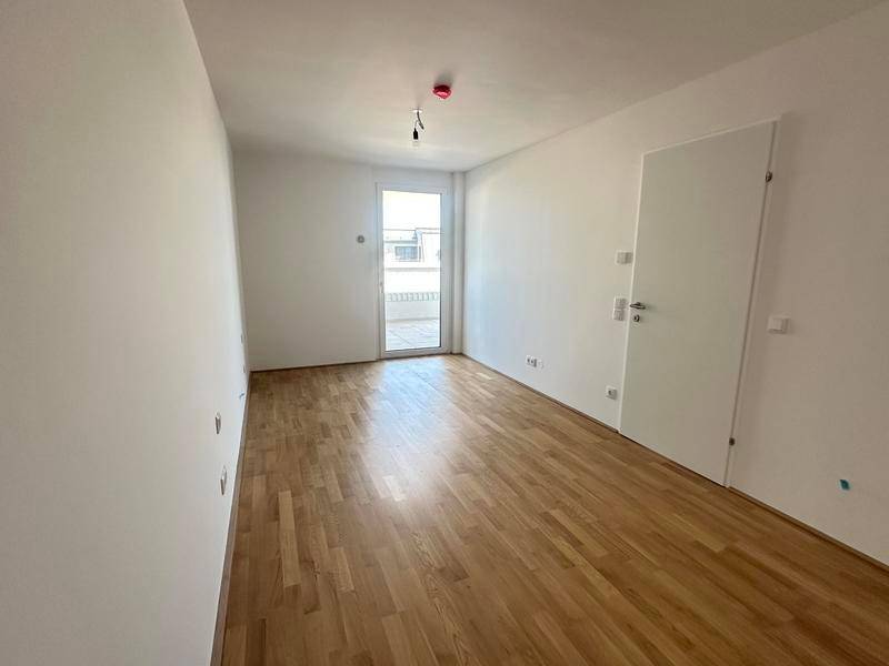 Helles Schlafzimmer mit Parkettboden, weißen Wänden und direktem Zugang zum Balkon.