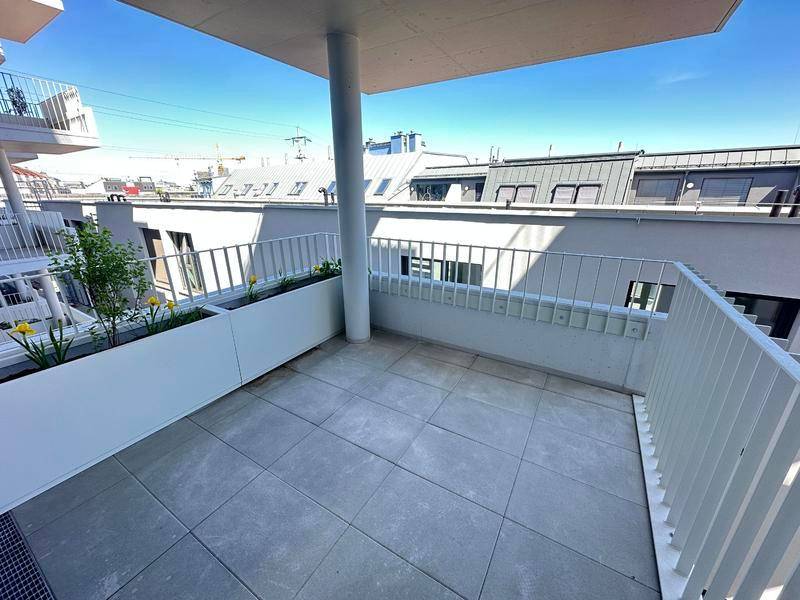 Heller Balkon mit Fliesenboden, weißem Geländer und Blick auf umliegende Gebäude.