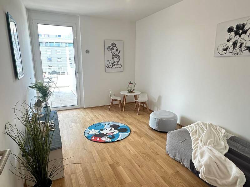 Helles Zimmer mit Holzboden und Zugang zu einem Balkon, dekoriert für Kinder.