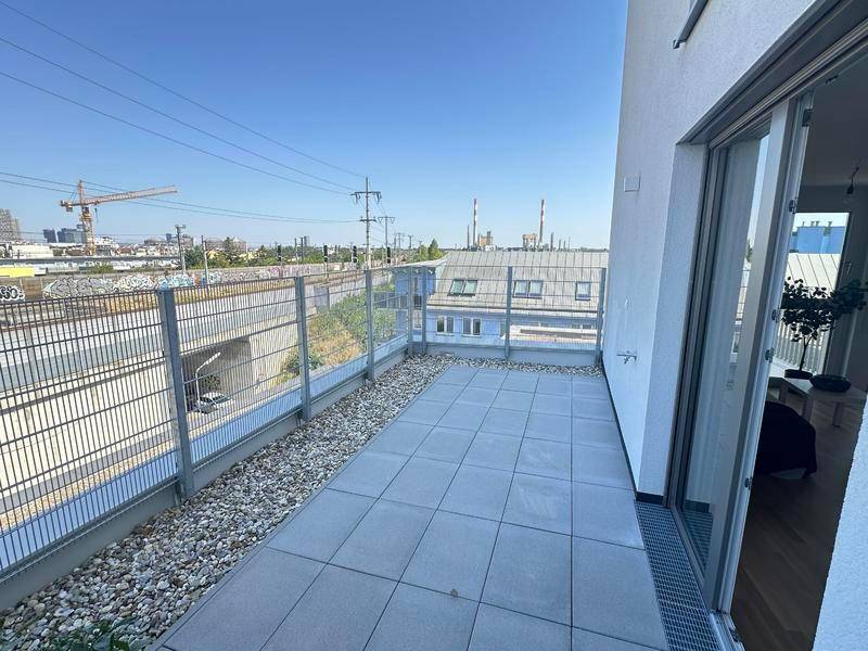 Lange, schmale Terrasse mit Fliesenboden und einem Blick auf Bahngleise und das Industriegebiet.