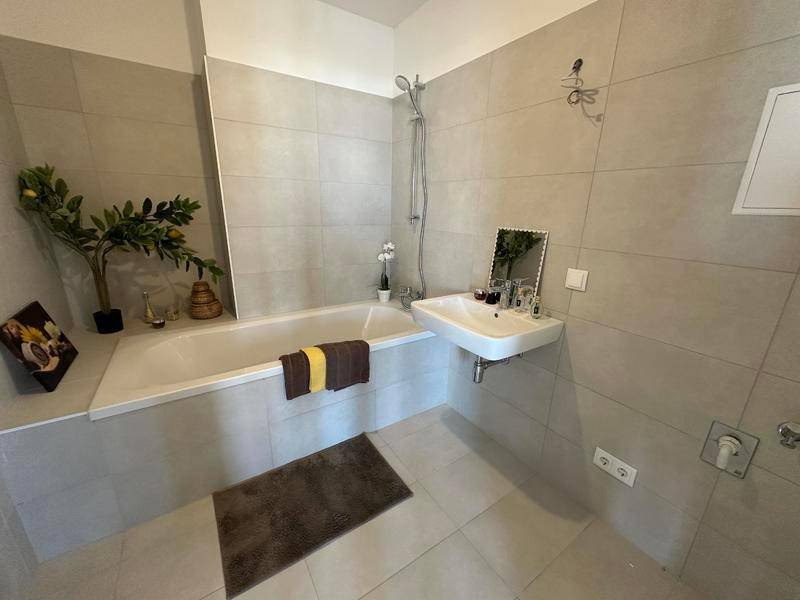 Modernes Badezimmer mit hellgrauen Fliesen, einer Badewanne und einem einzelnen Waschbecken.