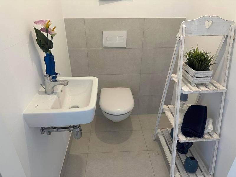 Modernes Gäste-WC mit Wand-WC, kleinem Waschbecken und hellen Fliesen an Wänden und Boden.
