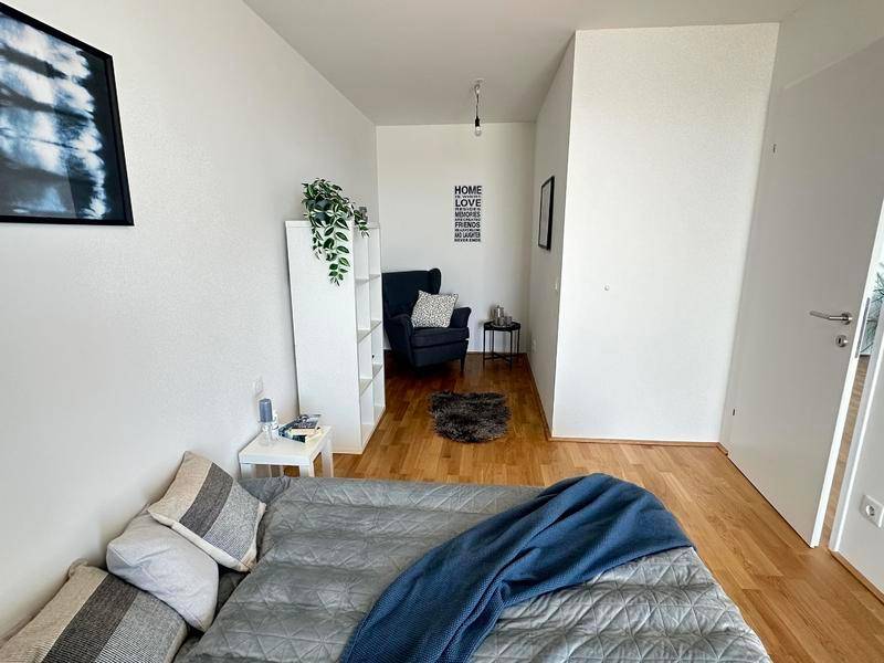 Schlafzimmer mit Holzboden und einer gemütlichen Leseecke, hell und modern gestaltet für Komfort.