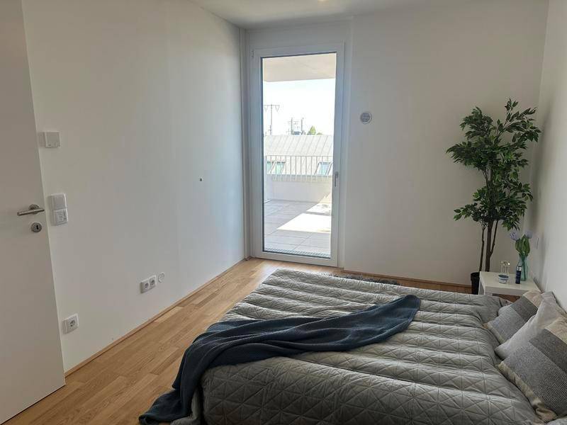 Helles Schlafzimmer mit Holzboden und direktem Zugang zu einem Außenbereich, minimalistisch eingerichtet.