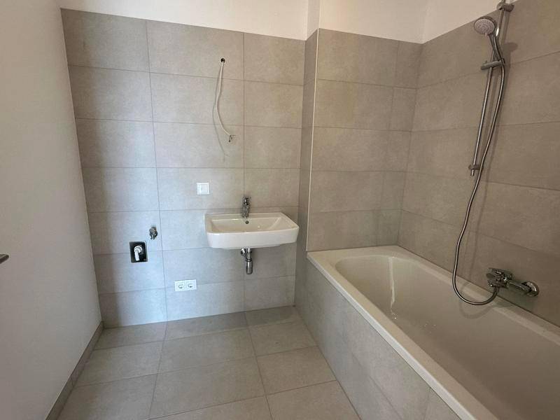 Unmöbliertes Badezimmer mit Badewanne, Waschbecken und hellen Fliesen an Wänden und Boden.