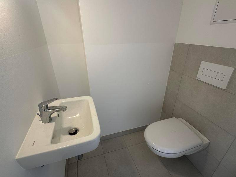 Modernes Gäste-WC mit wandhängendem WC, kleinem Waschbecken und Fliesenboden.