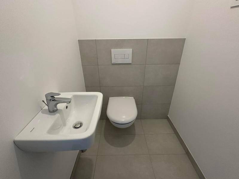 Separates WC mit wandhängender Toilette und kleinem Handwaschbecken.