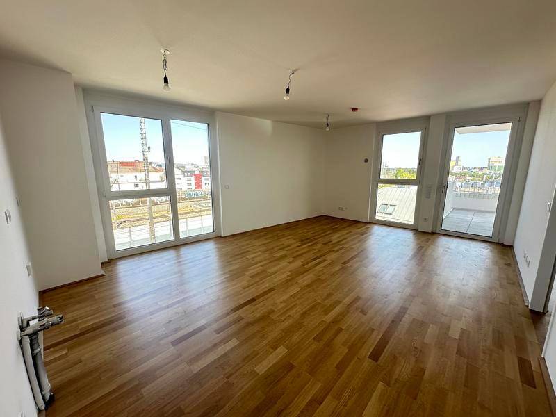 Helles, leeres Zimmer mit Parkettboden, großen Fenstern und Zugang zu einem Außenbereich.