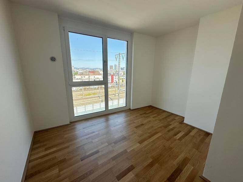 Leeres Schlafzimmer mit Eichenparkettboden und großem Fenster mit Blick auf die Umgebung.