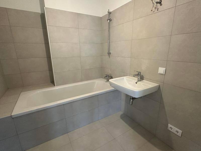 Modernes Badezimmer mit grauen Fliesen, Badewanne und Waschbecken.