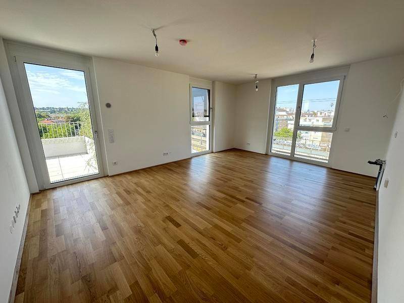 Heller Wohnraum mit Eichenparkettboden, großen Fenstern und Zugang zu einem Balkon.