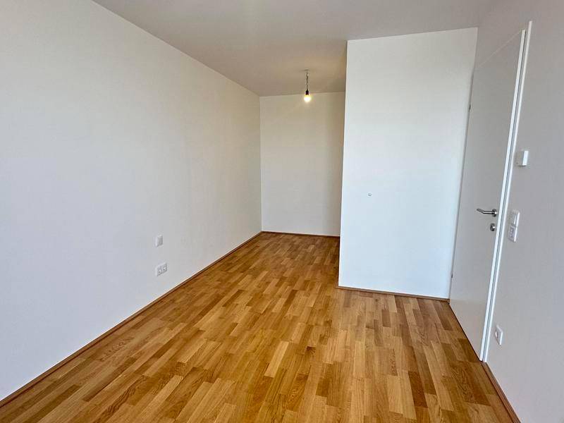 Leerer Raum mit Parkettboden und weiß gestrichenen Wänden, ideal als Arbeits- oder Gästezimmer.