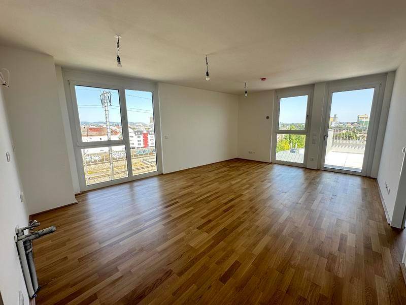 Heller, leerer Wohnraum mit Parkettboden und großen Fenstern mit Zugang zur Terrasse.