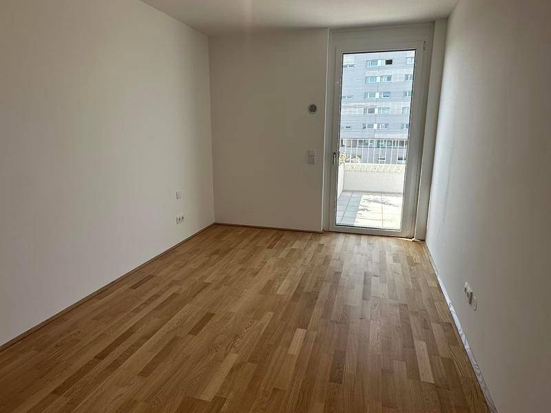 Helles Zimmer mit Holzboden und Zugang zu einem Außenbereich.
