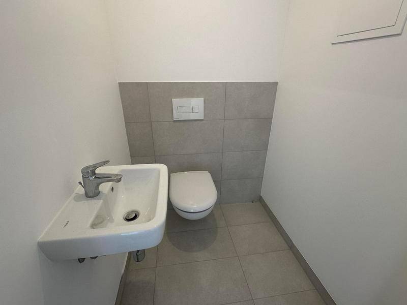Separates Gäste-WC mit Wand-WC und kleinem Waschbecken, in neutralen Farben gehalten.