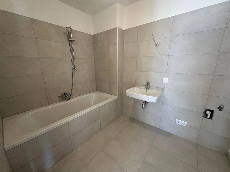 Modernes Badezimmer mit Badewanne, Waschbecken und grauen Fliesen.