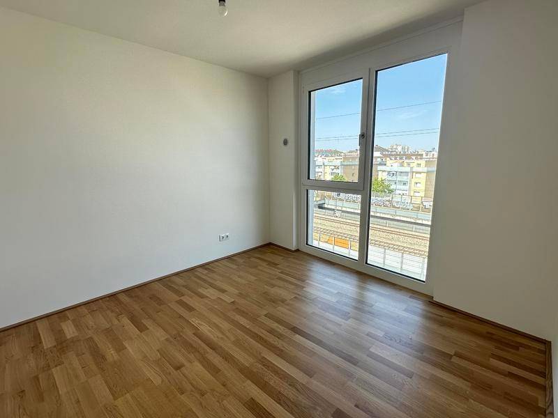 Leeres Schlafzimmer mit Parkettboden und großem Fenster mit Stadtblick.