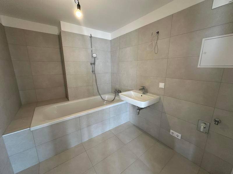 Modernes Badezimmer mit Badewanne, Dusche und hellgrauen Fliesen.