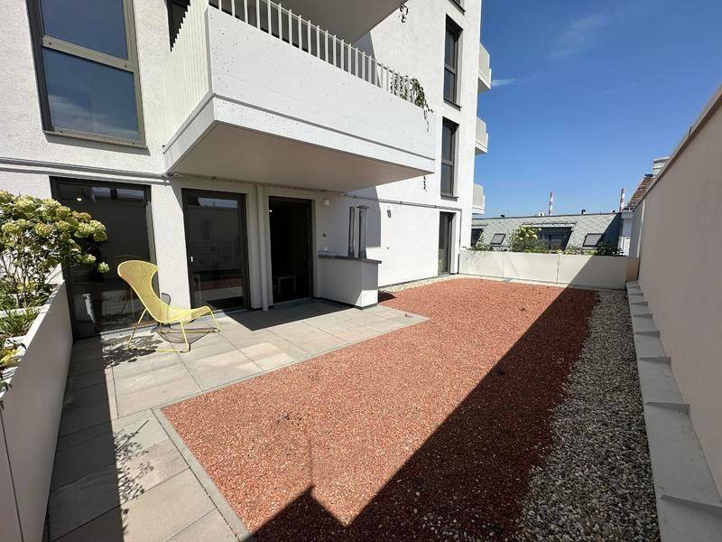 Geräumige Terrasse mit rotem Kies und einem Balkon darüber, ideal für Entspannung im Freien.