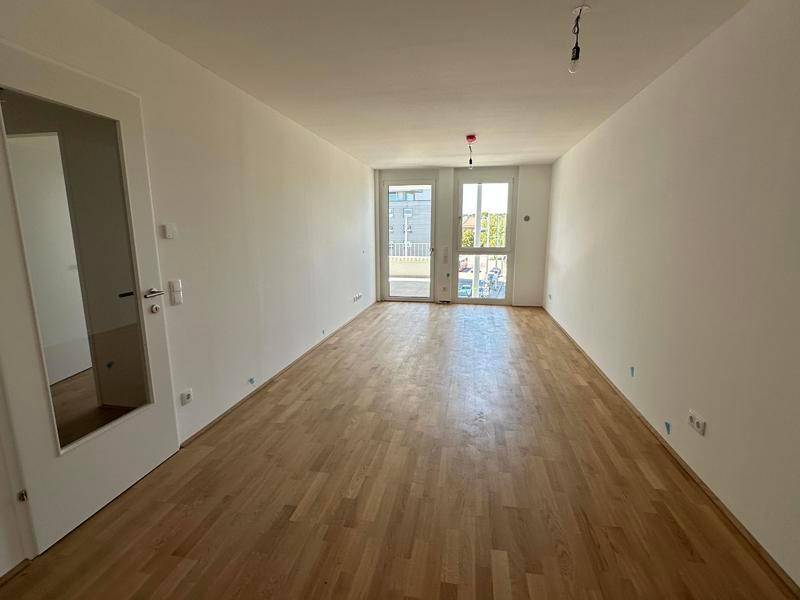 Heller, leerer Raum mit Parkettboden und Zugang zu einem Balkon oder einer Terrasse.