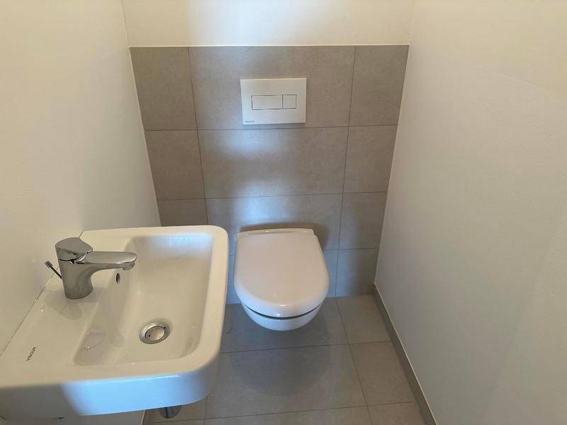 Kompaktes Gäste-WC mit Wand-WC und kleinem Waschbecken, modern gefliest.