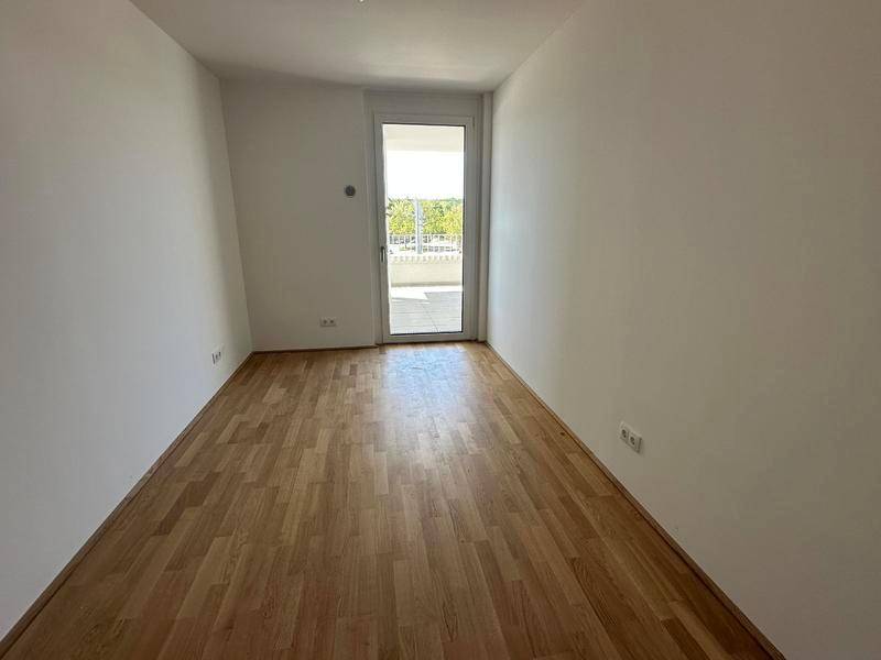 Helles Zimmer mit Parkettboden und einer Tür, die zu einem Balkon oder einer Terrasse führt.