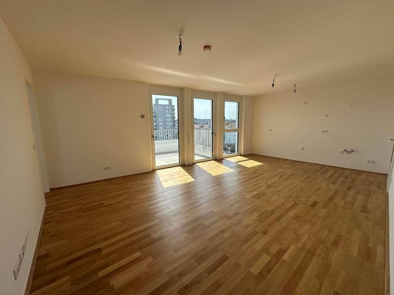 Heller, leerer Raum mit Holzboden und Zugang zu einem Balkon, der viel Tageslicht hereinlässt.