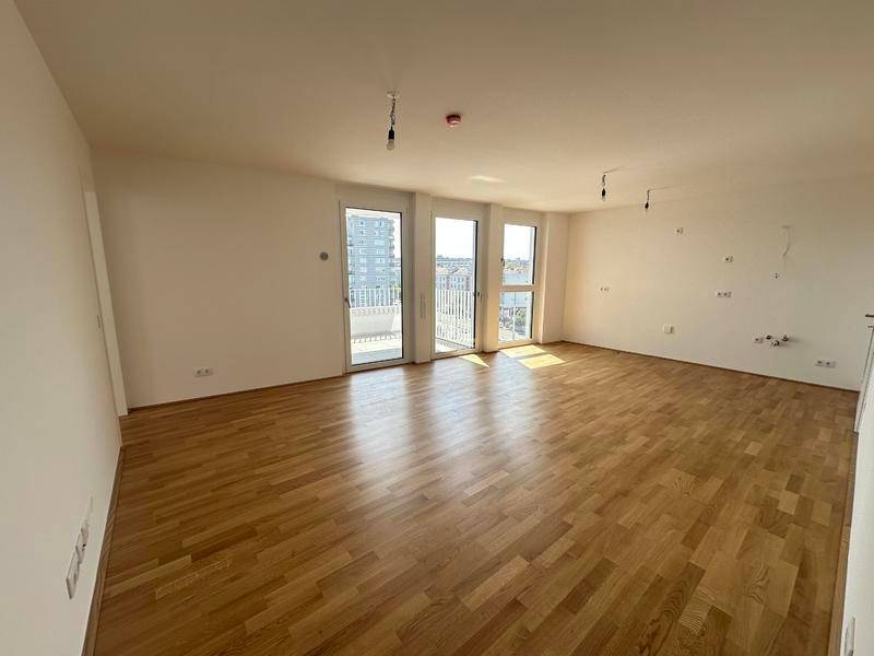 Heller, leerer Raum mit Holzboden und mehreren Fenstertüren zum Balkon.