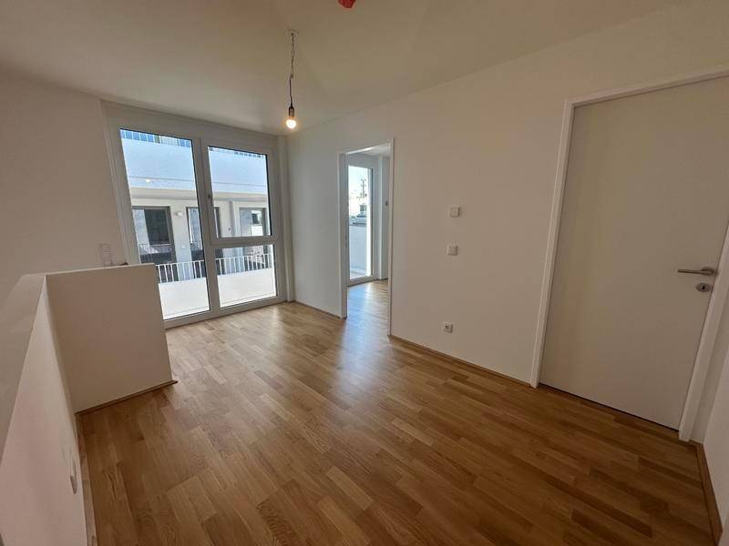 Heller Raum mit Holzparkettboden und Zugang zu einem Balkon oder einer Terrasse.
