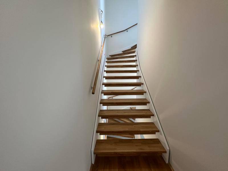 Moderne Holztreppe mit weißem Geländer, die verschiedene Ebenen verbindet.