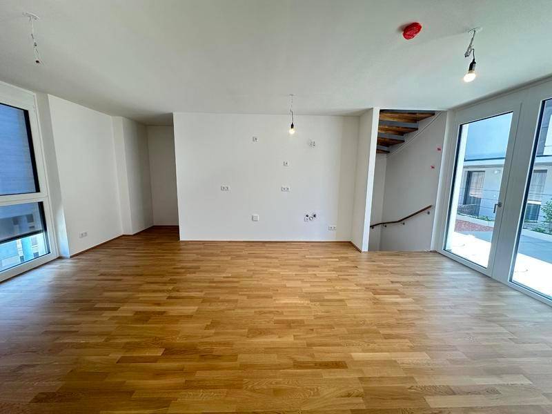 Geräumiger Wohnbereich mit Holzparkettboden und Zugang zu einer Treppe.
