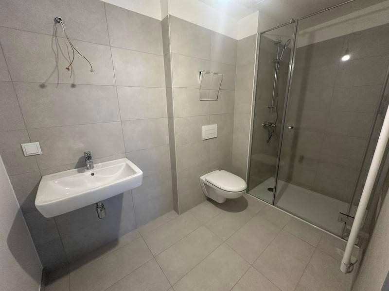 Modernes Badezimmer mit grauen Fliesen, wandhängendem WC und Duschkabine.