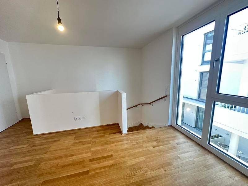 Heller Raum mit Holzparkettboden und Blick auf den Innenhof durch große Fenster.