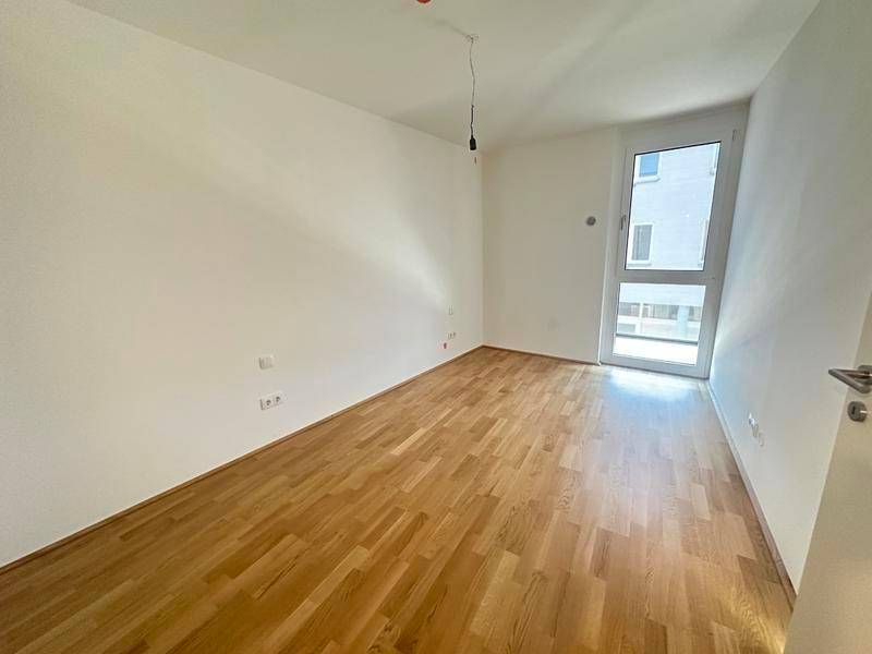 Helles Schlafzimmer mit Holzparkettboden und großem Fenster für viel Tageslicht.