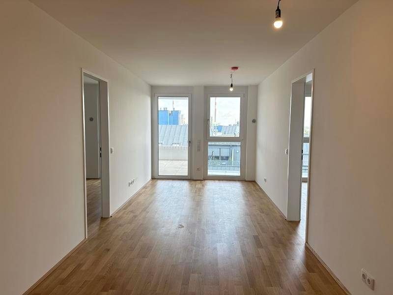 Heller, leerer Raum mit Holzboden und Zugang zu einem Außenbereich durch große Fenster.