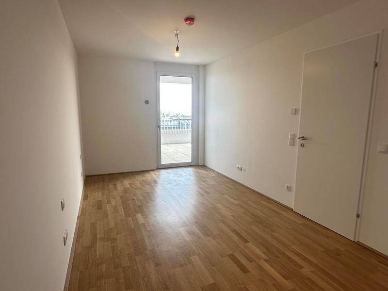 Heller Raum mit Holzboden und Zugang zu einem Balkon oder einer Terrasse, unmöbliert.