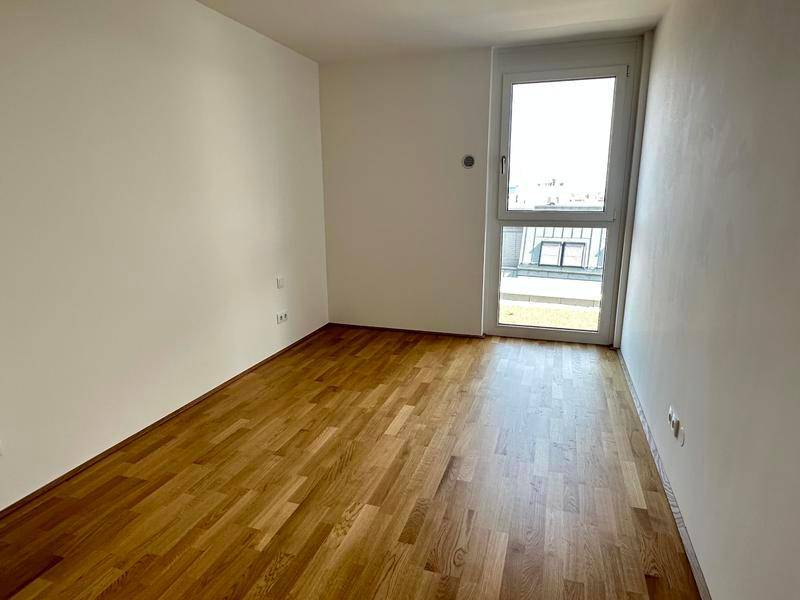 Schlafzimmer mit Holzboden, weißen Wänden und Zugang zu einem Balkon oder einer Terrasse.