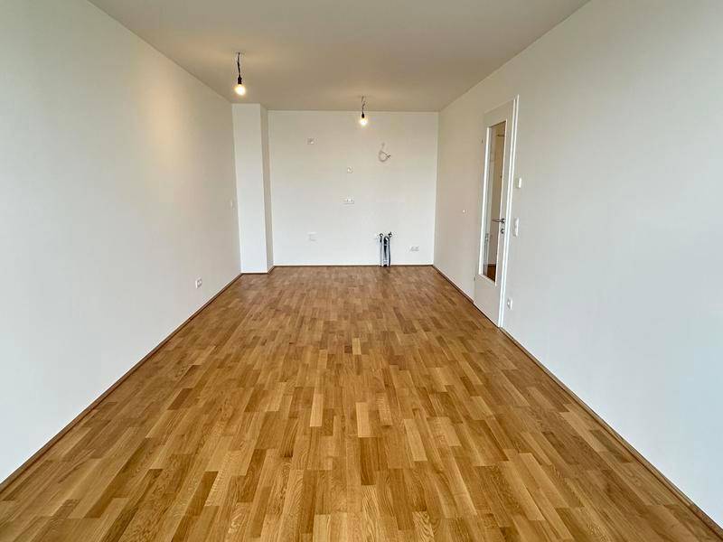 Leerer Raum mit Holzboden und Anschlüssen für eine zukünftige Einbauküche.