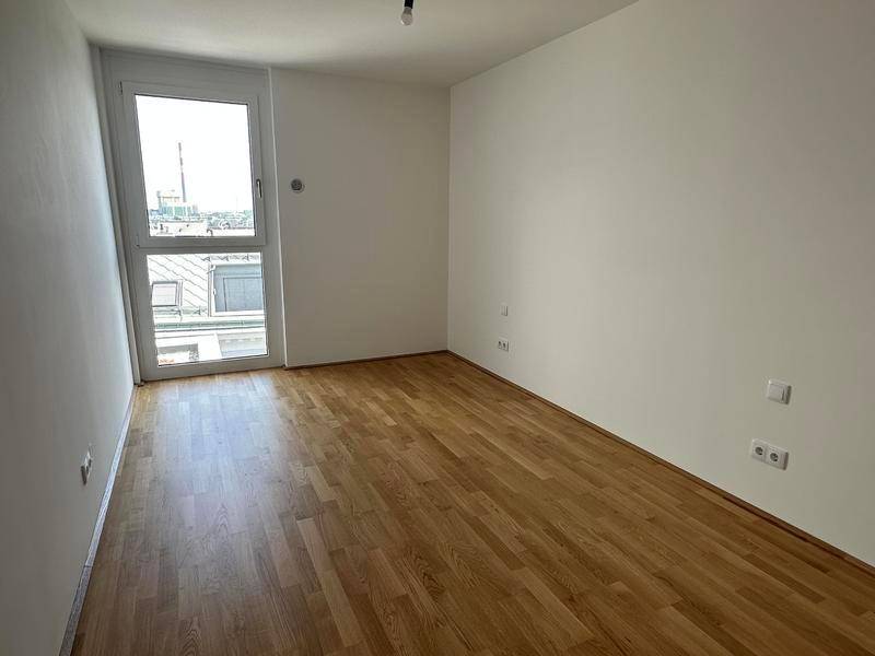 Helles, leeres Zimmer mit Parkettboden und großem Fenster, ideal als Schlaf- oder Arbeitszimmer.