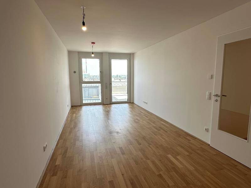 Heller, leerer Raum mit Parkettboden und Zugang zu einem Balkon oder einer Terrasse.