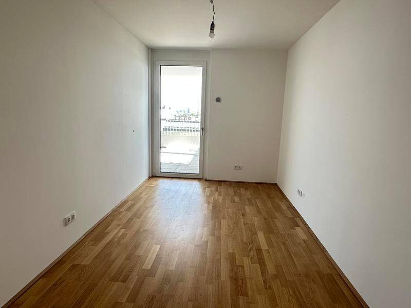 Leeres Schlafzimmer mit Parkettboden und Zugang zu einem Balkon oder einer Terrasse.