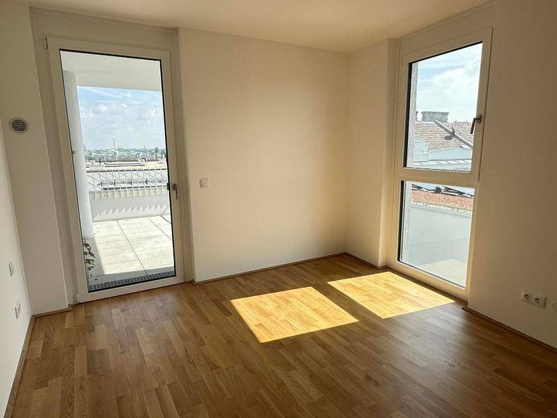 Helles Zimmer mit Holzboden und einer Fenstertür, die Zugang zu einem Balkon bietet.