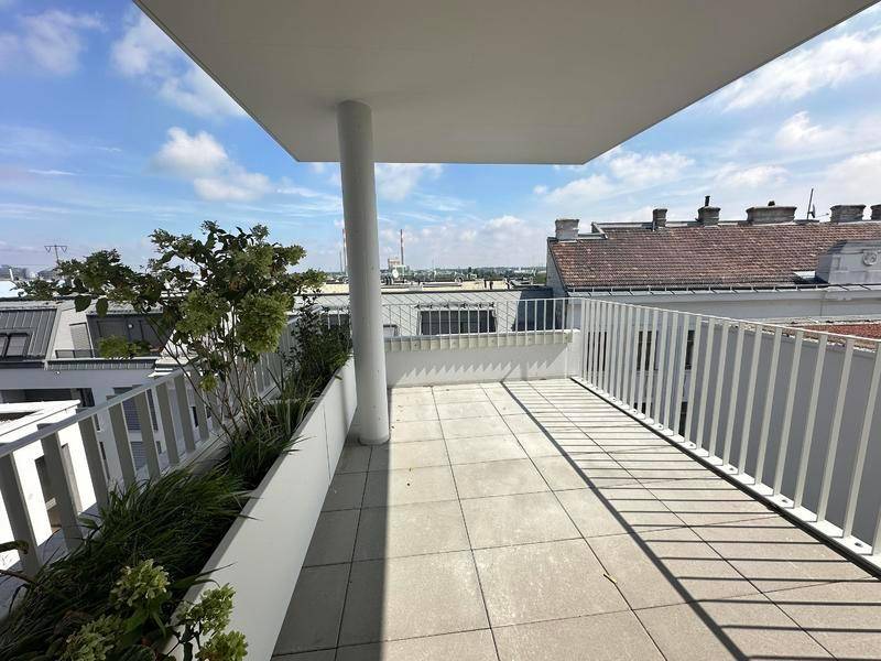 Sonniger Balkon mit Fliesenboden und Blick auf die umliegenden Gebäude und den Himmel.