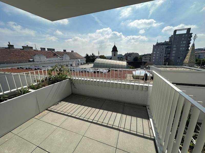 Balkon mit Fliesenboden und einem weiten Blick über die Dächer der Stadt und einen Kirchturm.