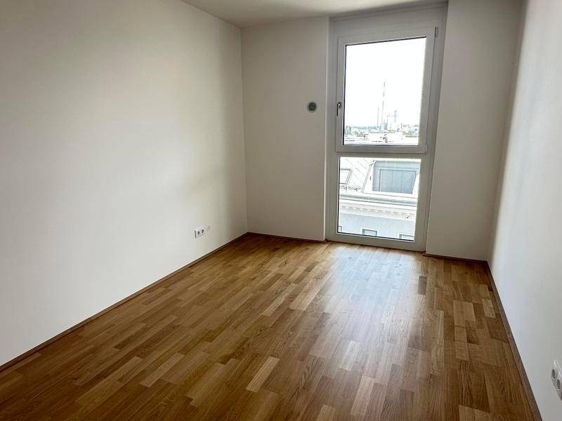 Kleines, helles Zimmer mit Holzboden und einem hohen Fenster, das einen Blick auf die Stadt bietet.
