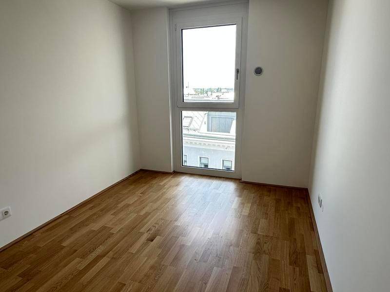 Helles Zimmer mit Holzboden und einem hohen Fenster, ideal als Kinder- oder Arbeitszimmer.