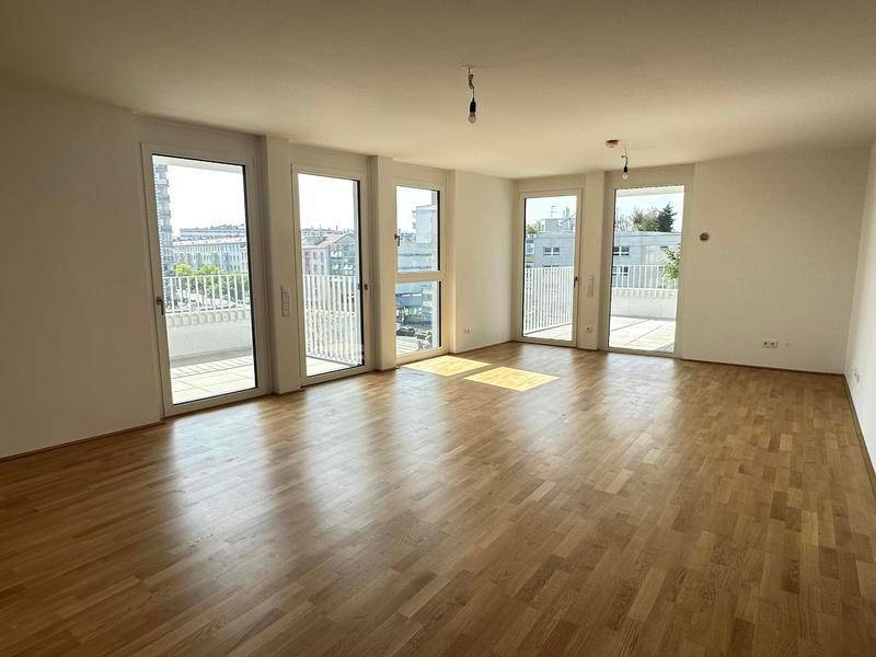 Heller, leerer Raum mit Parkettboden und mehreren Zugängen zu Balkonen.